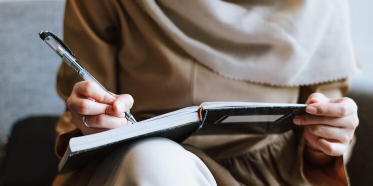 A smiling woman planning to conceive writing in a notebook with a fertility calendar in the background — representing preconception counseling and pregnancy planning at Walk In GYN Care