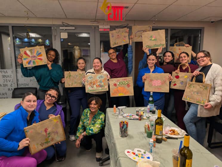 Walk In GYN Care staff members in New York holding hand-painted tote bags during a women’s wellness and team-building event.